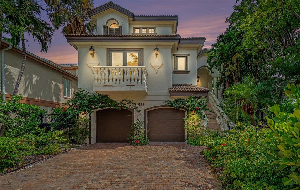 A two-story house with a balcony, two garage doors, and a brick driveway at dusk — 11523 ANDY ROSSE LANE, CAPTIVA, FL