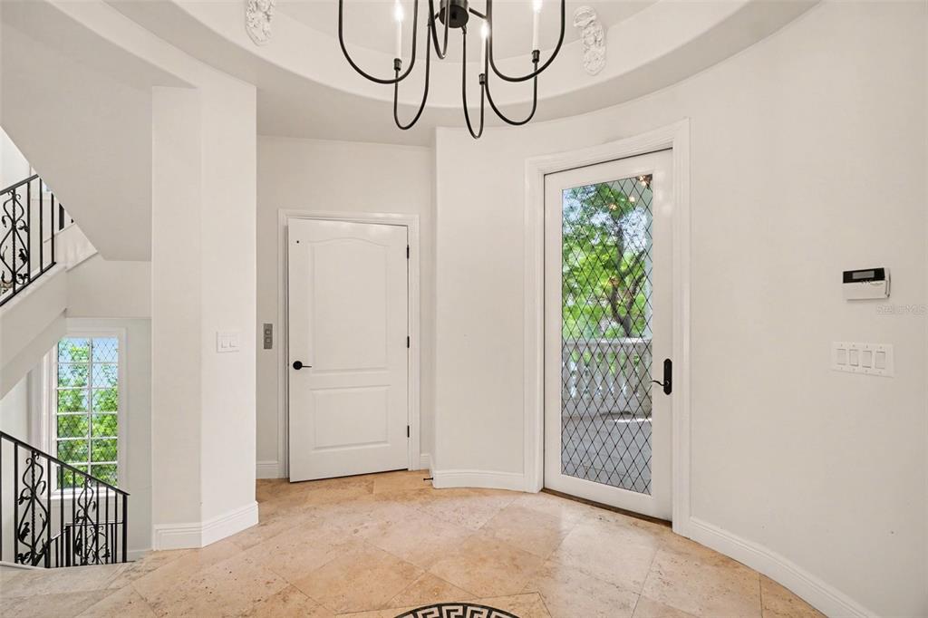 A bright foyer features a chandelier, tiled floor, staircase with iron railing, and glass door — 11523 ANDY ROSSE LANE, CAPTIVA, FL