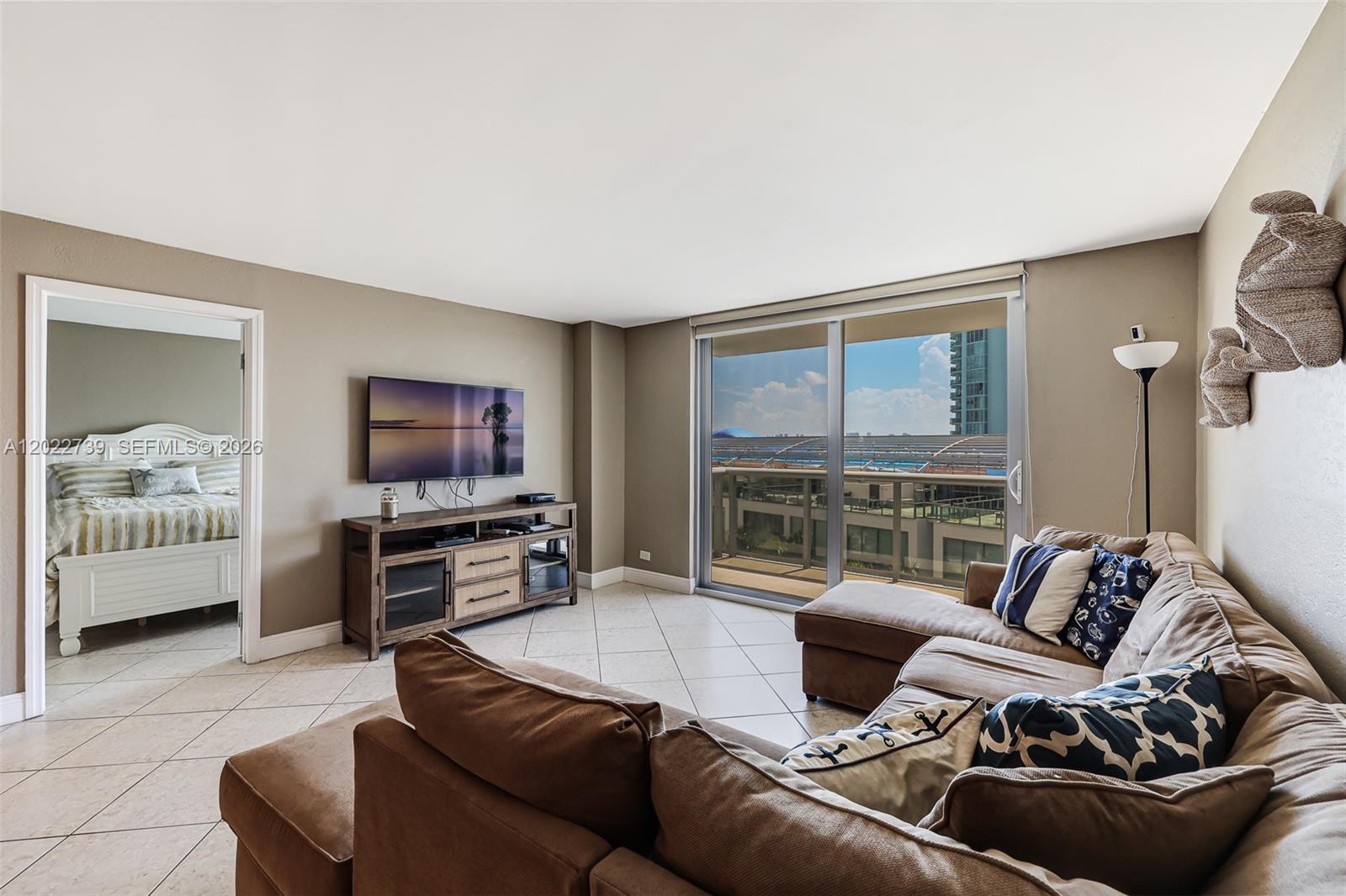 A living room features a brown sectional sofa, a television, and a balcony with views — 6039 Collins Ave # 936, Miami Beach FL 33140, MIAMI BEACH, FL