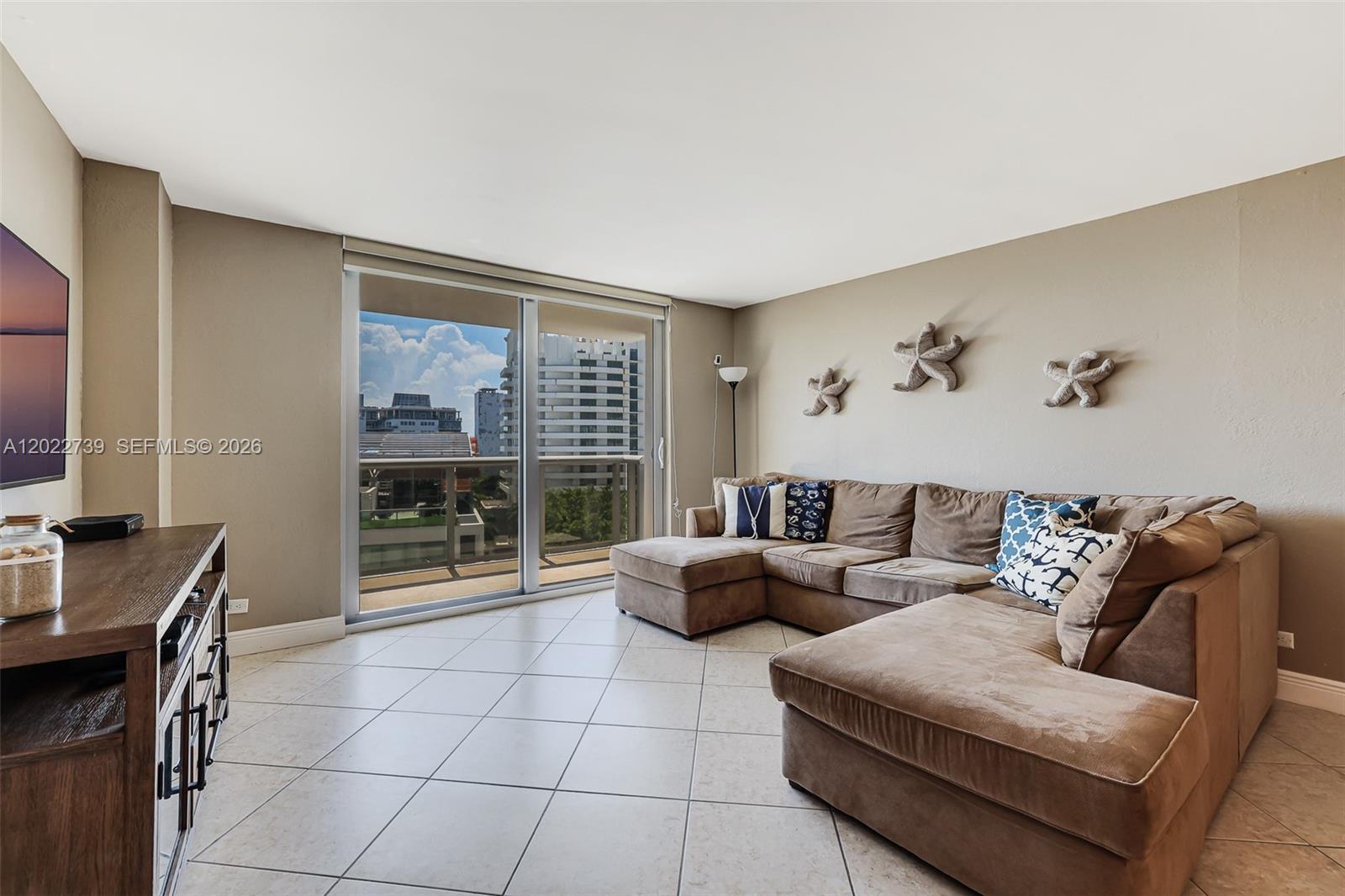 A living room features a brown sectional sofa, tile floors, and a sliding glass door — 6039 Collins Ave # 936, Miami Beach FL 33140, MIAMI BEACH, FL
