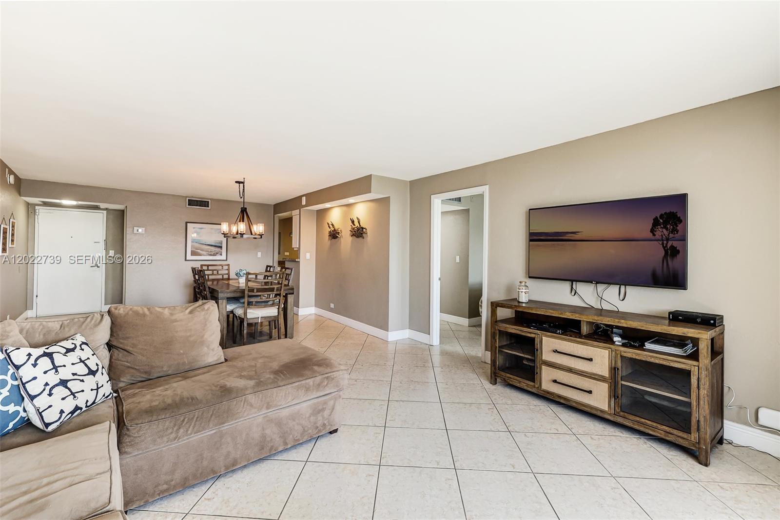 A living room features a beige sectional sofa, a wooden media console, and a dining area — 6039 Collins Ave # 936, Miami Beach FL 33140, MIAMI BEACH, FL
