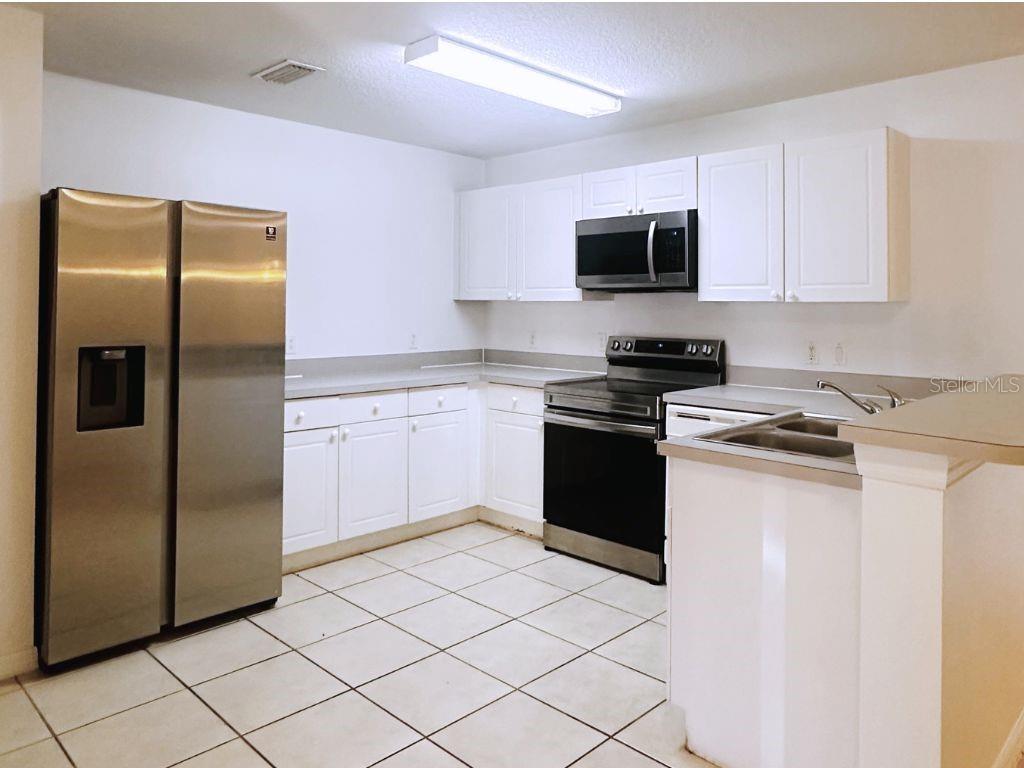 A kitchen with white cabinets, stainless steel appliances, and light-colored tile flooring — 2770 CLUB CORTILE CIRCLE UNIT A, KISSIMMEE, FL