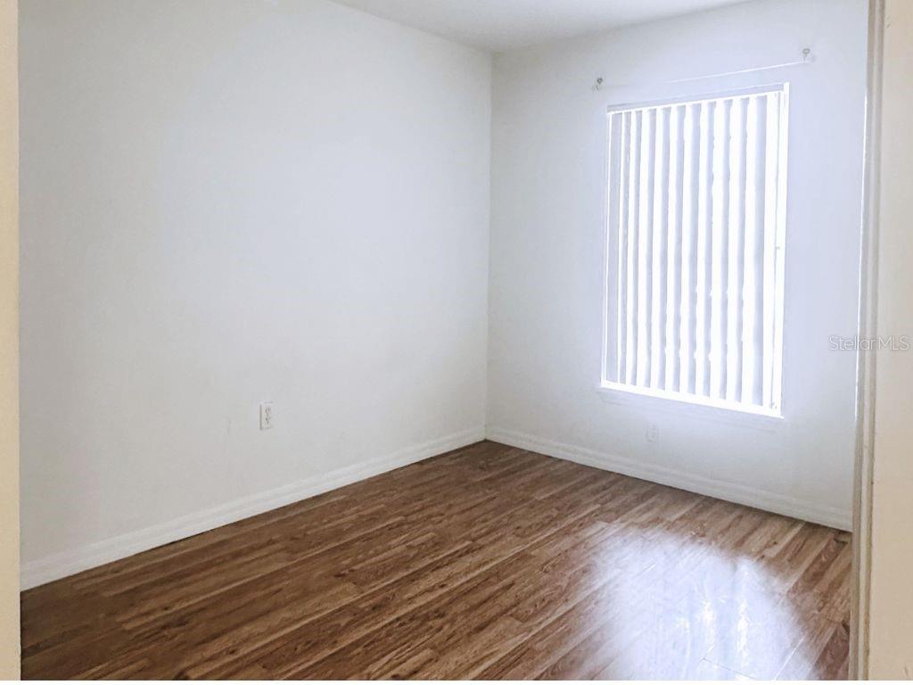 An empty room with white walls, wood-look flooring, and a window with vertical blinds — 2770 CLUB CORTILE CIRCLE UNIT A, KISSIMMEE, FL