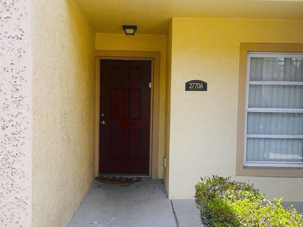 A red front door is set into a yellow stucco exterior wall with a window — 2770 CLUB CORTILE CIRCLE UNIT A, KISSIMMEE, FL