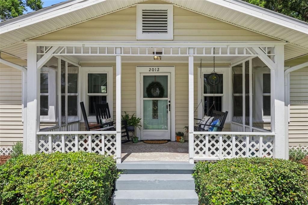 A front porch with a white lattice railing, rocking chairs, and a hanging swing — 2012 S PALMETTO AVENUE, SANFORD, FL