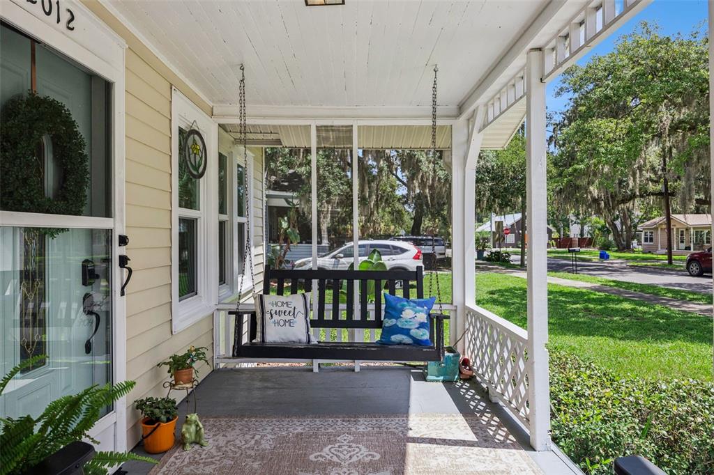 A covered front porch features a black hanging swing, a patterned rug, and lattice railings — 2012 S PALMETTO AVENUE, SANFORD, FL
