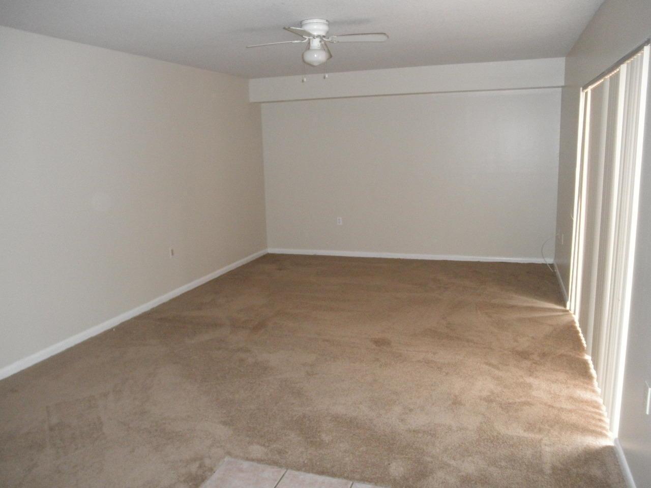 An empty living room with beige carpet, neutral walls, and a ceiling fan — WEST PALM BEACH, FL