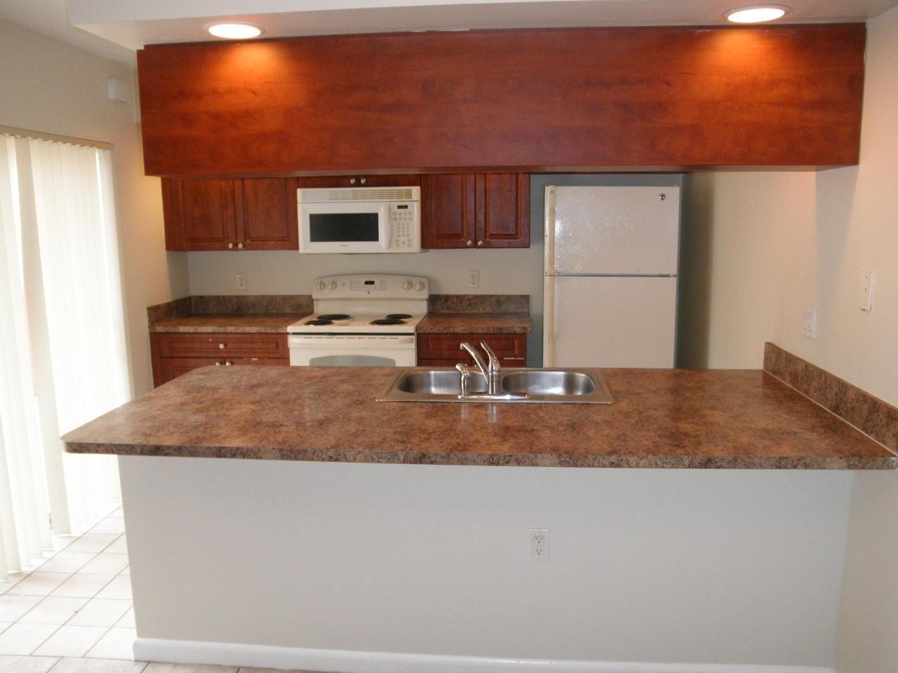 A kitchen features wood cabinets, a white stove, a white refrigerator, and a laminate countertop — WEST PALM BEACH, FL