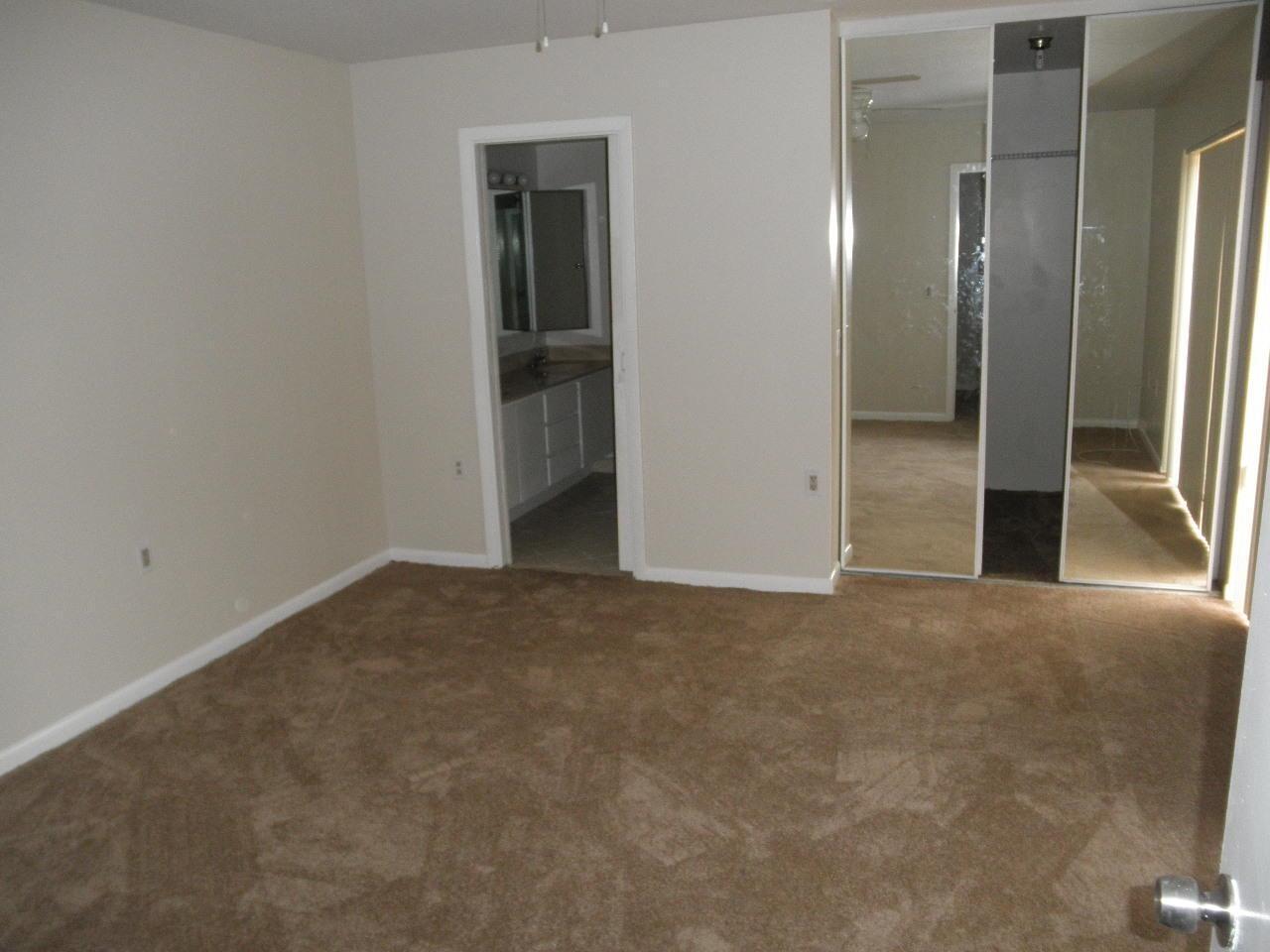 A bedroom with beige carpet, light-colored walls, a doorway to a bathroom, and mirrored closets — WEST PALM BEACH, FL