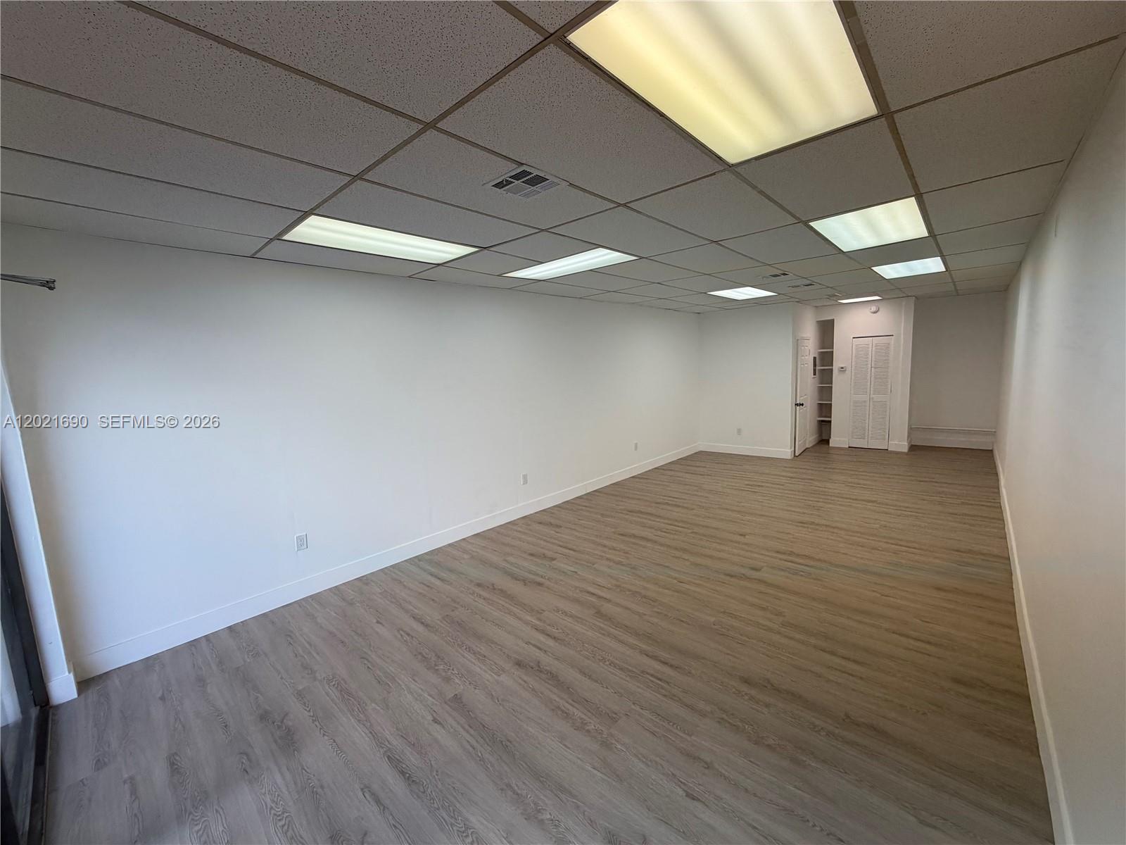 An empty office space features white walls, a drop ceiling with recessed lighting, and wood-look flooring — 517 SW 12th Ave, Miami FL 33130, MIAMI, FL