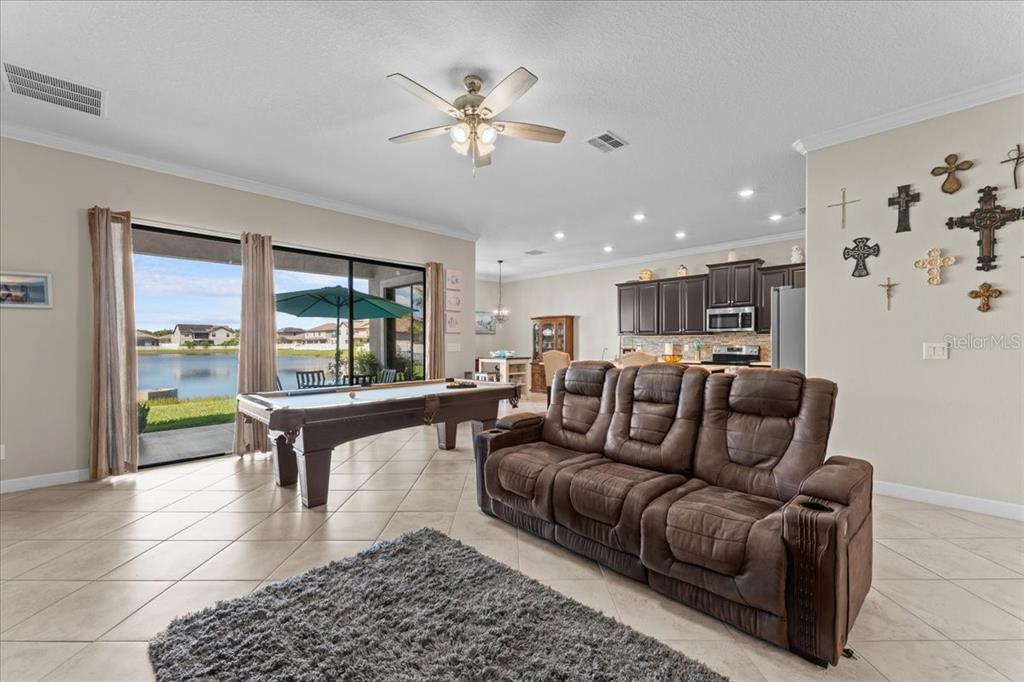 A living room with a pool table, brown leather sofa, and sliding doors overlooking a lake — 13443 WHITE SAPPHIRE ROAD, RIVERVIEW, FL