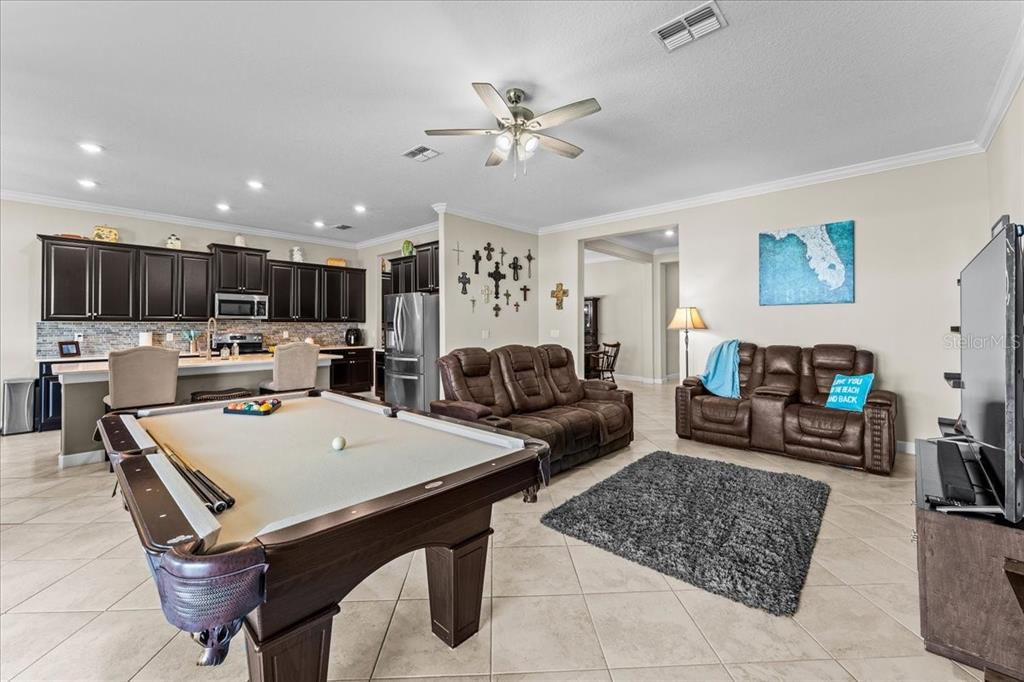 A living room and kitchen area features a pool table, brown sofas, and dark cabinetry — 13443 WHITE SAPPHIRE ROAD, RIVERVIEW, FL
