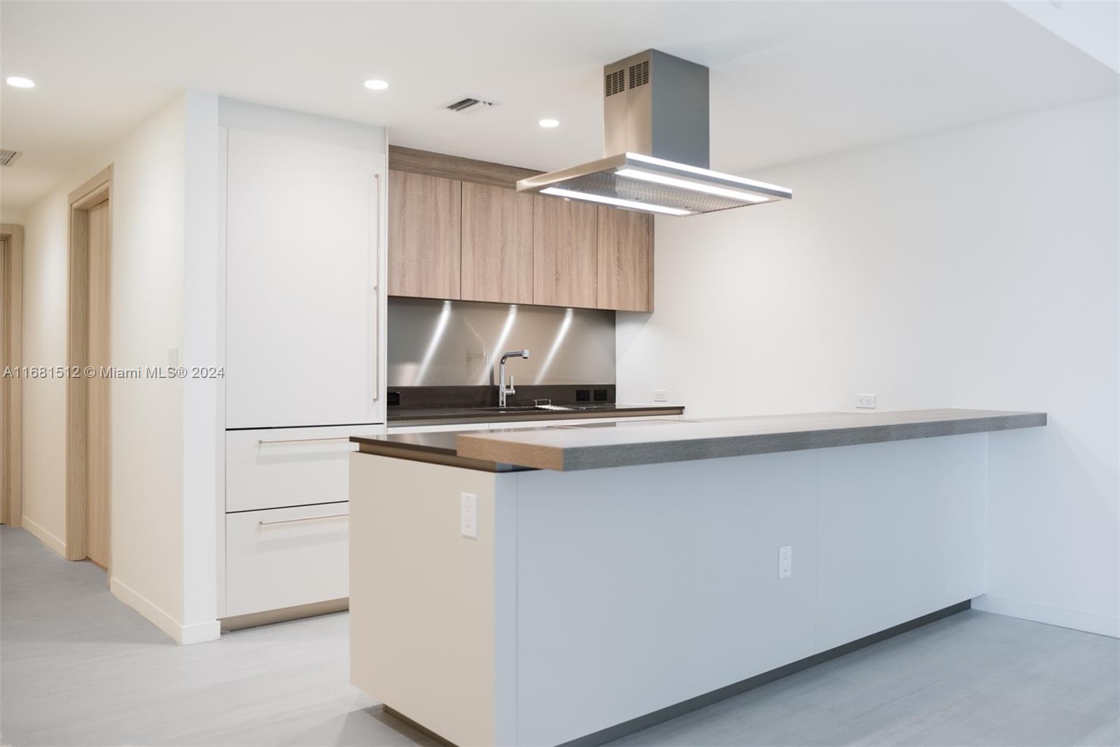 A modern kitchen features white cabinetry, wood-toned upper cabinets, a stainless steel hood, and an island — 1000 Brickell Plaza # 3307, Miami FL 33131, MIAMI, FL