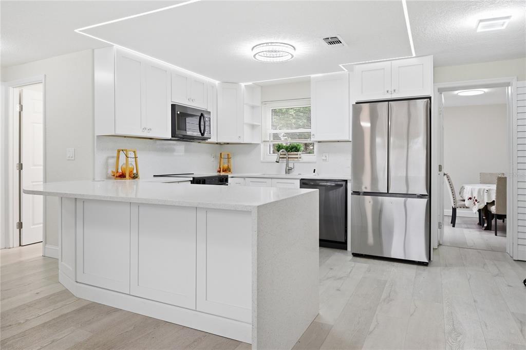 A modern kitchen features white cabinets, a quartz island, and stainless steel appliances — 6338 ABERDEEN AVENUE, NEW PORT RICHEY, FL