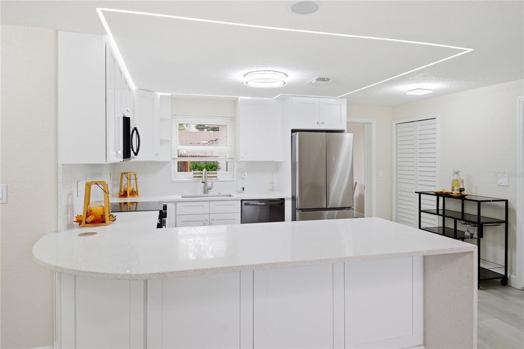 A white kitchen features a curved island, stainless steel appliances, and recessed ceiling lighting — 6338 ABERDEEN AVENUE, NEW PORT RICHEY, FL