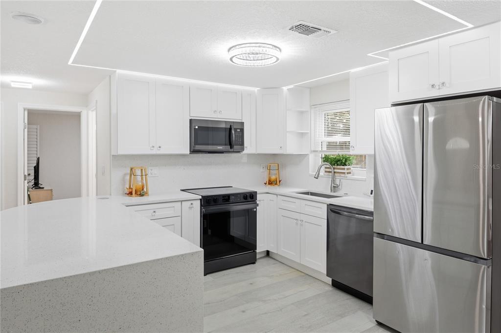 A modern kitchen features white cabinets, stainless steel appliances, and a large quartz-topped island — 6338 ABERDEEN AVENUE, NEW PORT RICHEY, FL