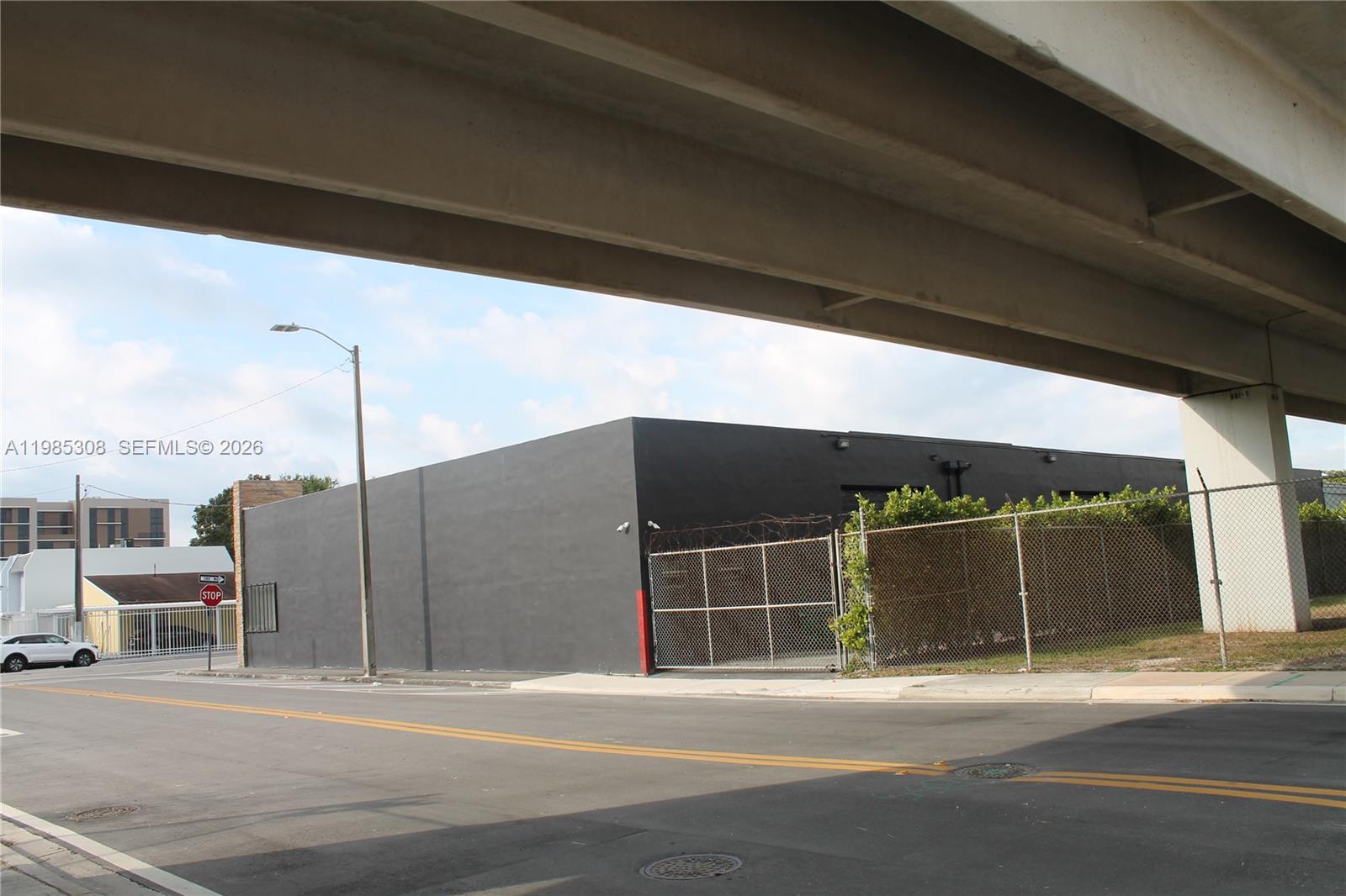 A black industrial building sits beneath an overpass next to a chain-link fence — 601 NW 11th St, Miami FL 33136, MIAMI, FL
