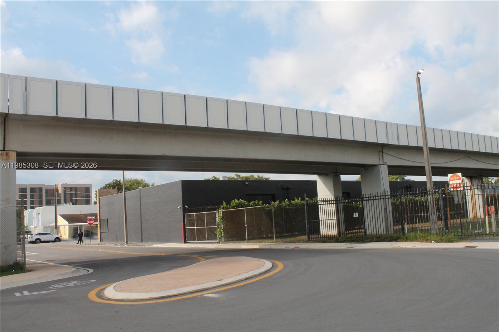 An elevated highway overpass spans above a paved road and a fenced industrial building — 601 NW 11th St, Miami FL 33136, MIAMI, FL