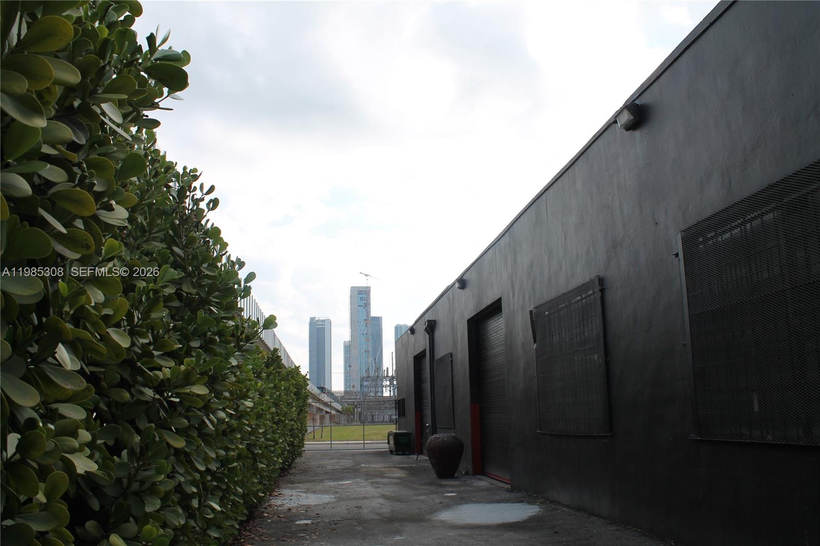A paved exterior walkway runs alongside a black building wall and a tall green hedge — 601 NW 11th St, Miami FL 33136, MIAMI, FL