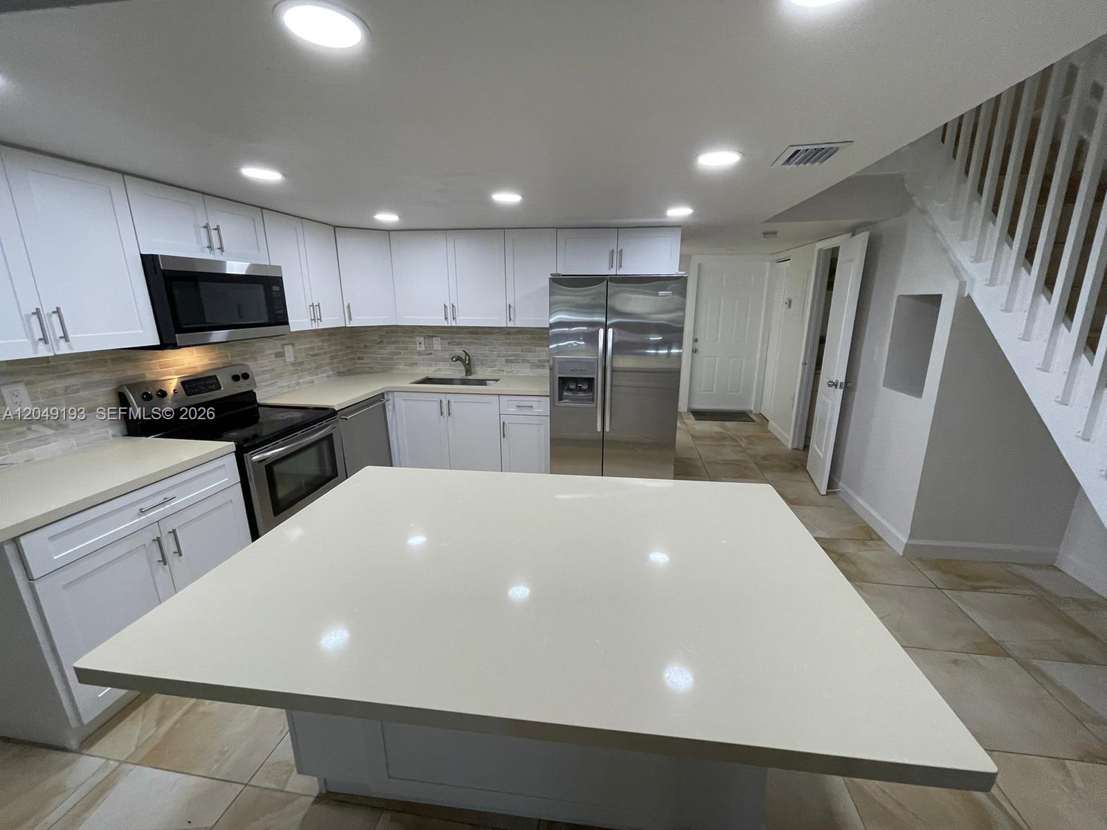 A kitchen features white cabinetry, stainless steel appliances, a large island, and light-colored tile flooring — 13037 SW 88th Ln # 204A, Miami FL 33186, MIAMI, FL