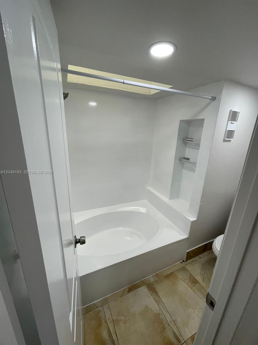 A bathroom features a white soaking tub with a showerhead and built-in wall shelving — 13037 SW 88th Ln # 204A, Miami FL 33186, MIAMI, FL