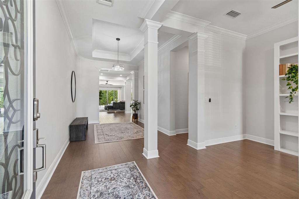A bright entryway features white columns, hardwood floors, a tray ceiling, and built-in shelving — 4000 BLUE LANTANA LANE, LAND O LAKES, FL