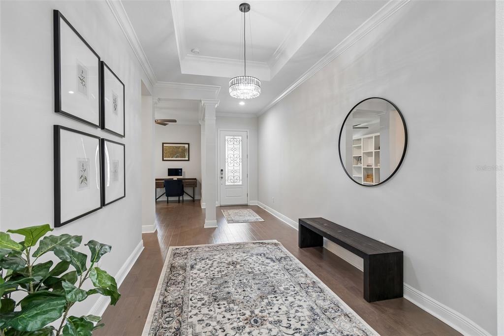 A bright entryway features a tray ceiling, a crystal chandelier, hardwood floors, and a bench — 4000 BLUE LANTANA LANE, LAND O LAKES, FL