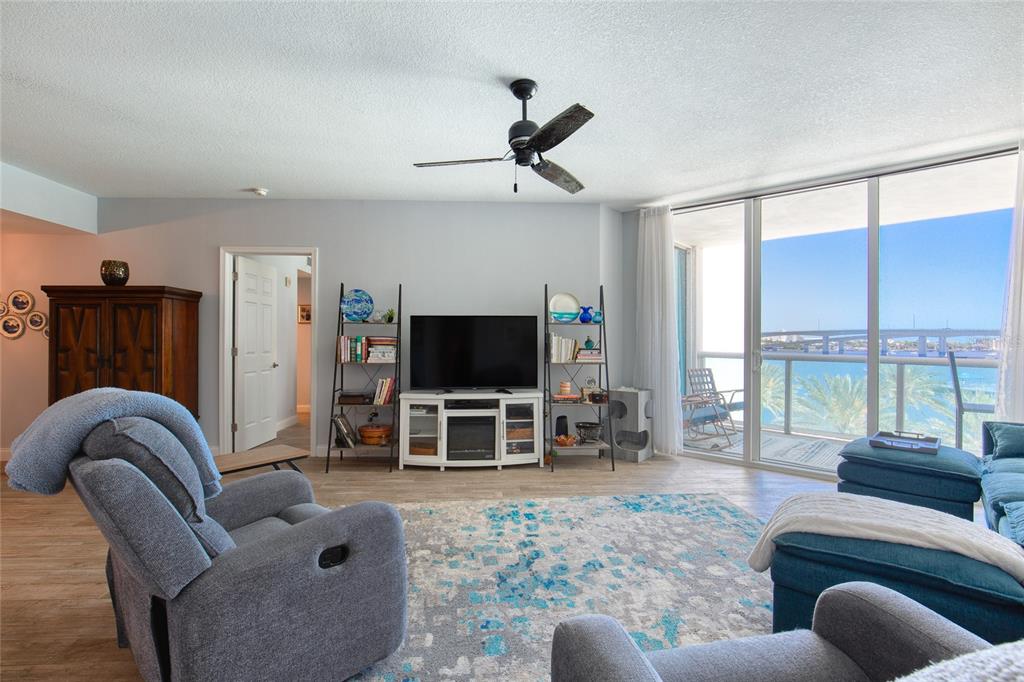 A living room features a television, shelving, blue furniture, and a balcony overlooking the water — 241 RIVERSIDE DRIVE UNIT 405, HOLLY HILL, FL