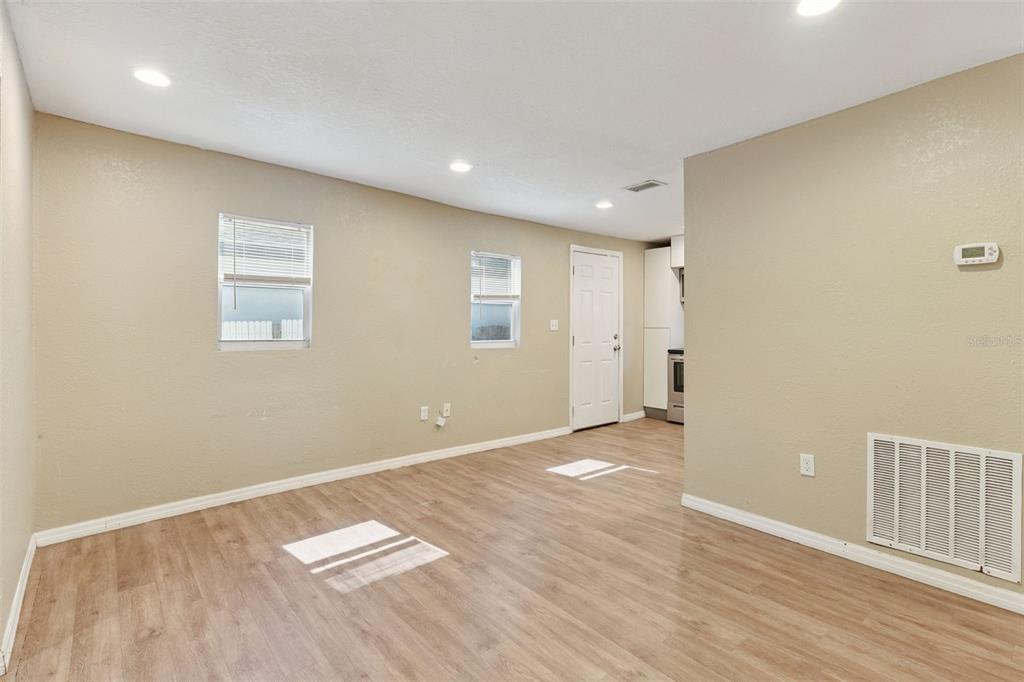 An empty room with light wood-look flooring, beige walls, two windows, and a white door — 5000 HUPPEL AVENUE, ORLANDO, FL