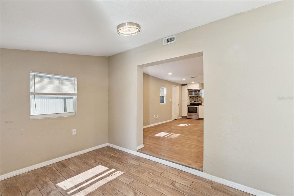 A room with wood-look tile flooring leads through a wide opening into a kitchen — 5000 HUPPEL AVENUE, ORLANDO, FL