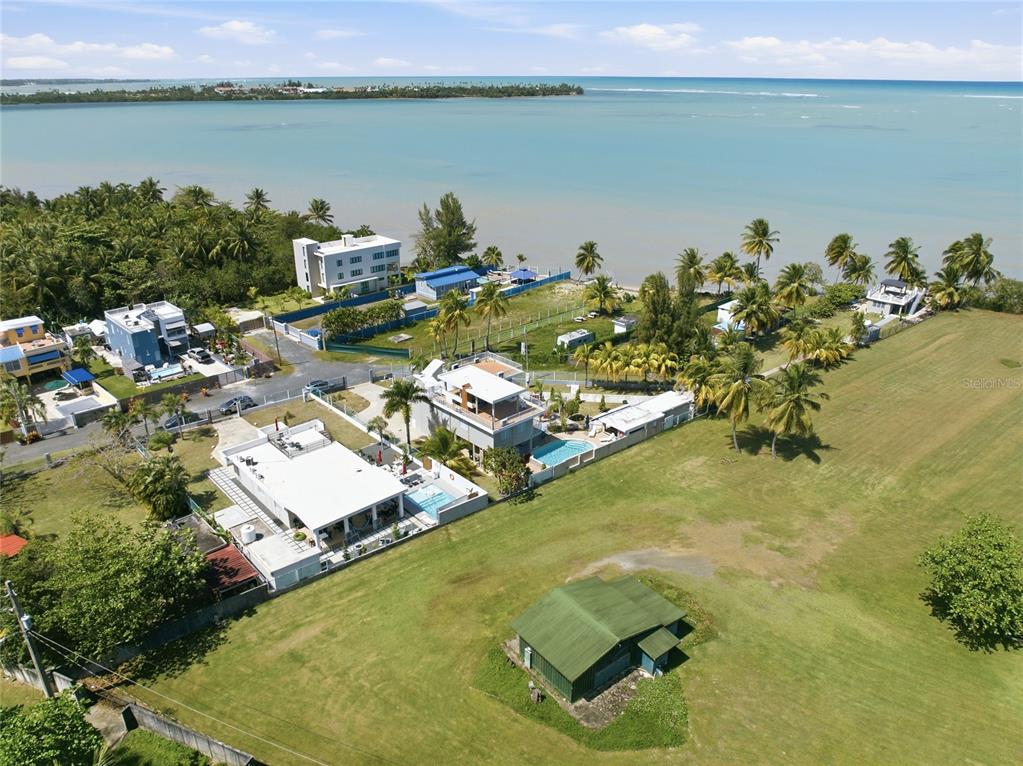 An aerial view shows several coastal houses with swimming pools near a grassy field — Pr 968k 2.1 int Punta Are LAS PICUAS, RIO GRANDE, PR