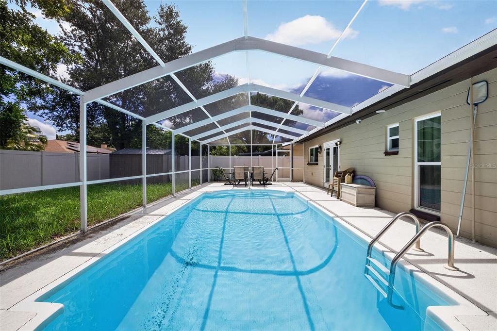 A rectangular swimming pool is enclosed by a white screen cage in a backyard — 1977 CITRUS HILL ROAD, PALM HARBOR, FL