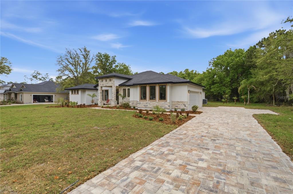 A modern single-story house with a stone facade, white siding, and a paved driveway — 1516 PINE ISLAND ROAD, KISSIMMEE, FL