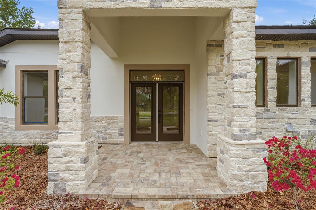 A stone-pillared entryway features a paved porch leading to a set of double glass doors — 1516 PINE ISLAND ROAD, KISSIMMEE, FL