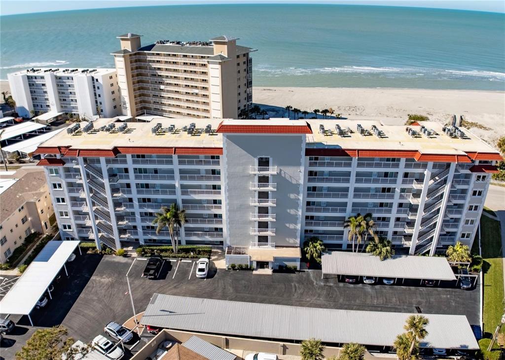 An aerial view shows a multi-story beachfront condominium building with covered parking and palm trees — 500 THE ESPLANADE N UNIT 306, VENICE, FL