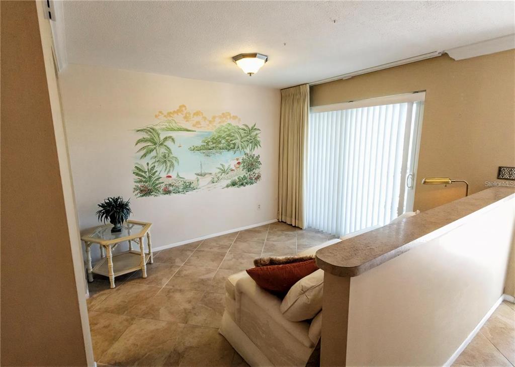 A living room features tile flooring, a tropical wall mural, and a sliding glass door — 500 THE ESPLANADE N UNIT 306, VENICE, FL
