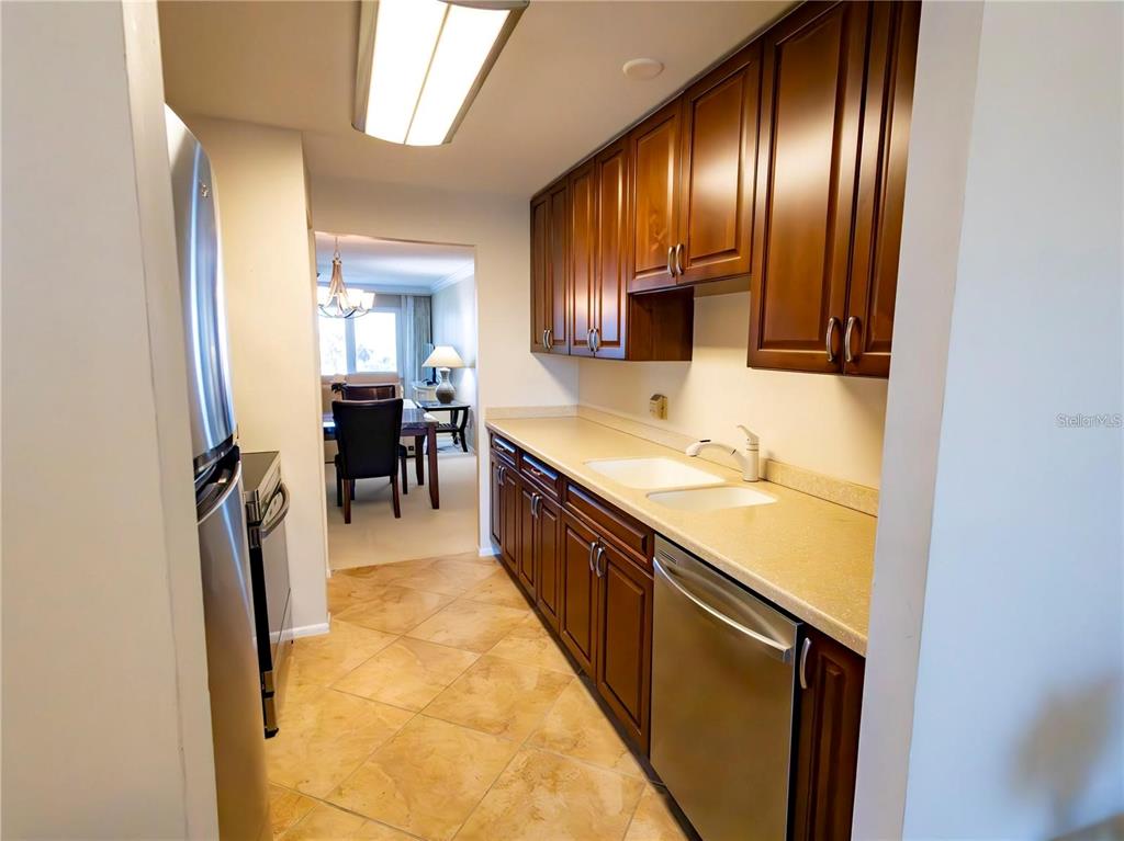 A galley kitchen features wood cabinets, stainless steel appliances, and tile flooring — 500 THE ESPLANADE N UNIT 306, VENICE, FL