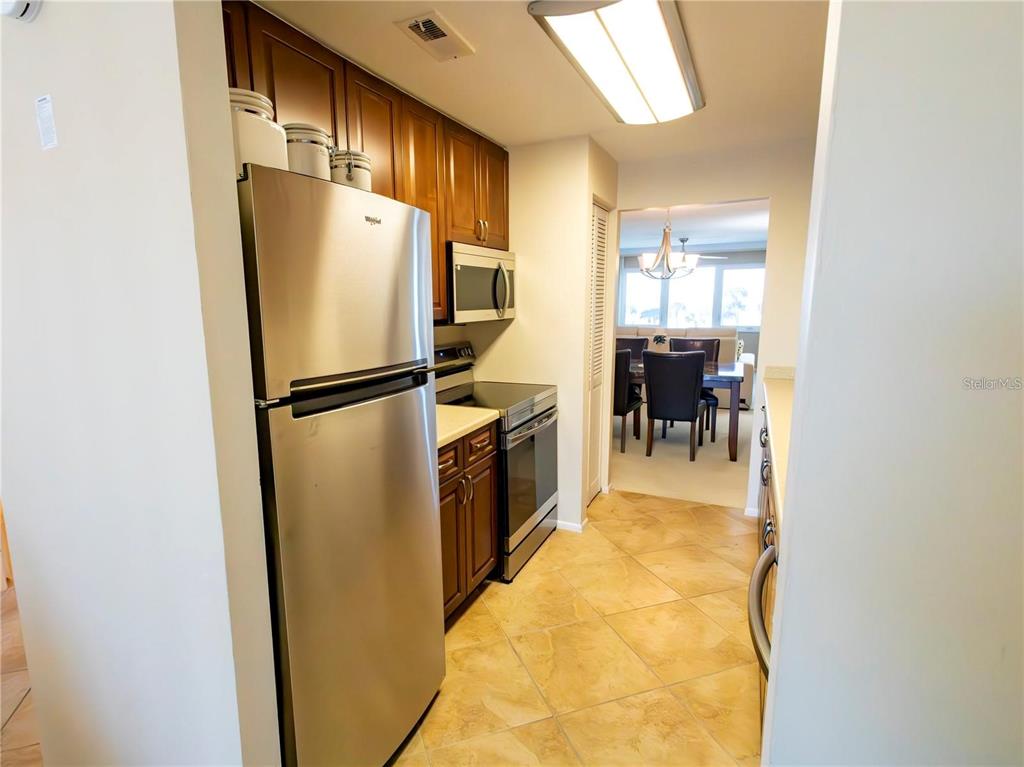 A galley kitchen features stainless steel appliances, wood cabinets, and light-colored tile flooring — 500 THE ESPLANADE N UNIT 306, VENICE, FL