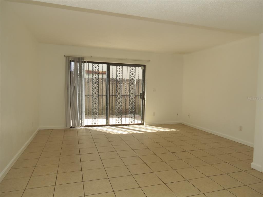 An empty living room features beige tile flooring, white walls, and a sliding glass door — 625 N HALIFAX AVENUE UNIT 6, DAYTONA BEACH, FL