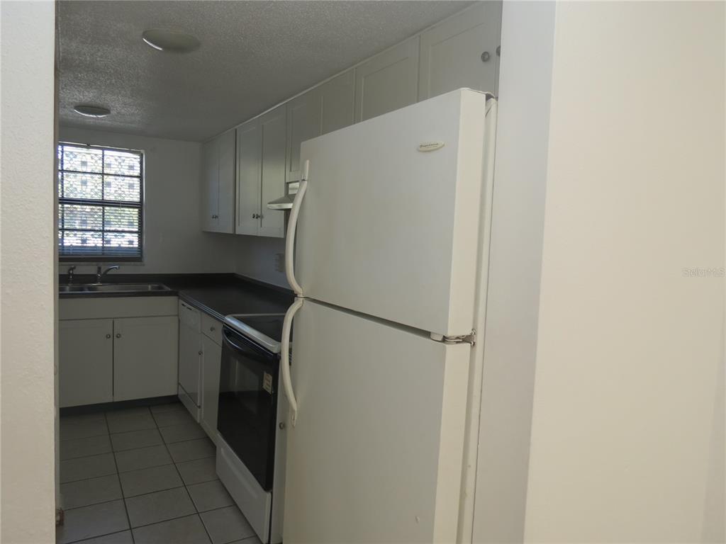 A kitchen features white cabinets, a white refrigerator, a black stove, and tiled flooring — 625 N HALIFAX AVENUE UNIT 6, DAYTONA BEACH, FL
