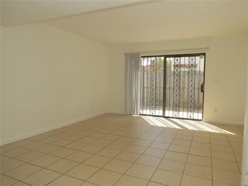 An empty room features light-colored floor tiles, white walls, and a sliding glass door — 625 N HALIFAX AVENUE UNIT 6, DAYTONA BEACH, FL