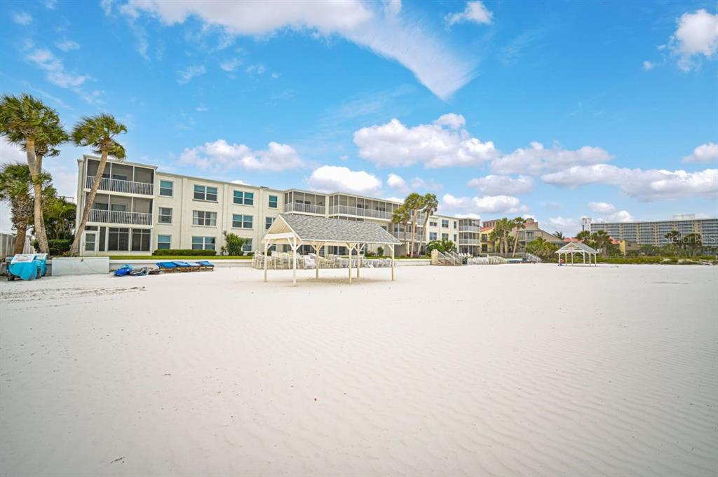 A multi-story apartment building sits behind a white sand beach with two wooden gazebos — 6154 MIDNIGHT PASS ROAD UNIT D13, SARASOTA, FL