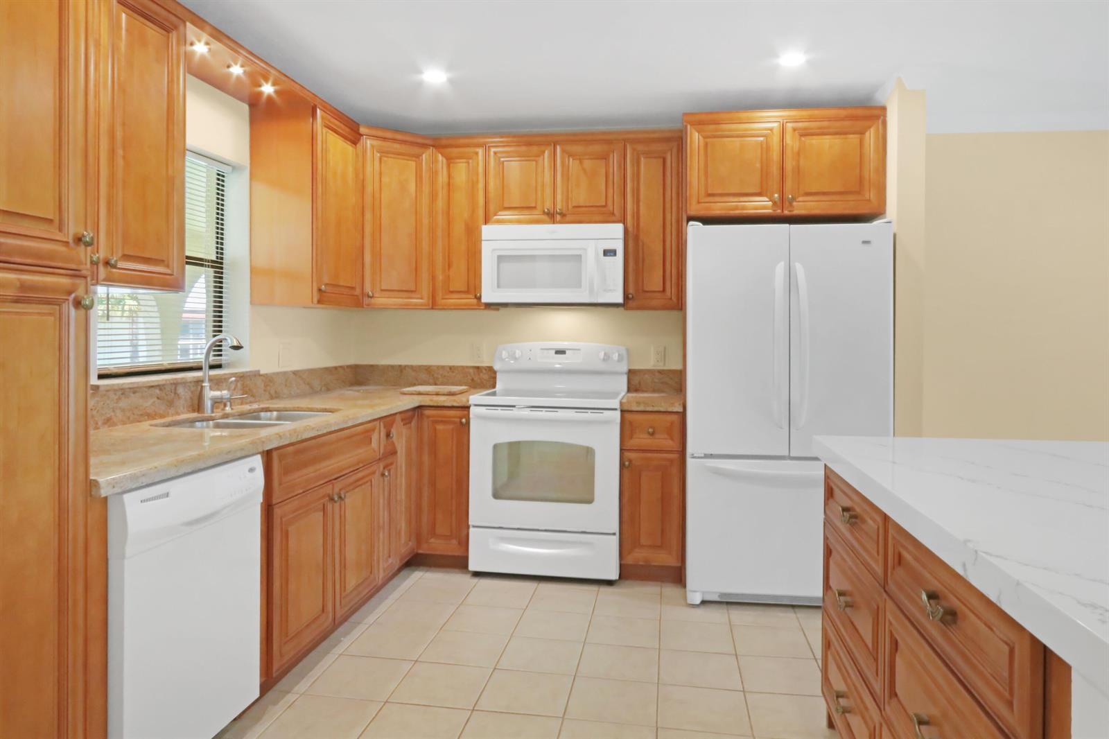 A kitchen with wood cabinets, white appliances, beige tile floors, and granite countertops — 717 S Us Hwy 1 # 712, Jupiter FL 33477, JUPITER, FL