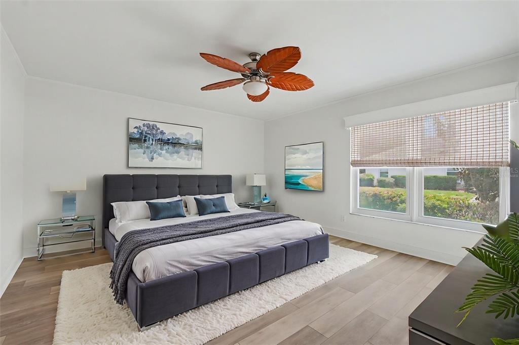 A bedroom features a tufted gray bed, wood-look flooring, a palm-leaf ceiling fan, and large windows — 8359 CANDLEWOOD ROAD UNIT 8359, SEMINOLE, FL