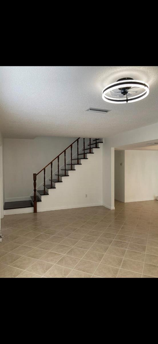 A room with tile flooring, a staircase with a dark wood railing, and a ceiling fan — 1243 Kinglet Terrace, Wellington FL 33414, WELLINGTON, FL