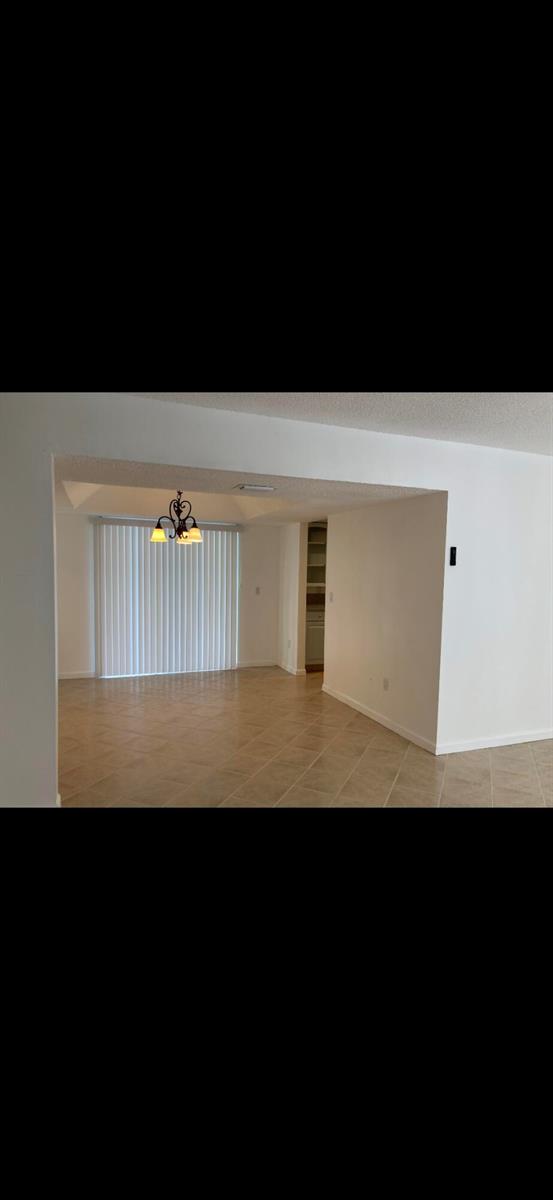 An empty dining area features tile flooring, a chandelier, and vertical blinds over sliding doors — 1243 Kinglet Terrace, Wellington FL 33414, WELLINGTON, FL