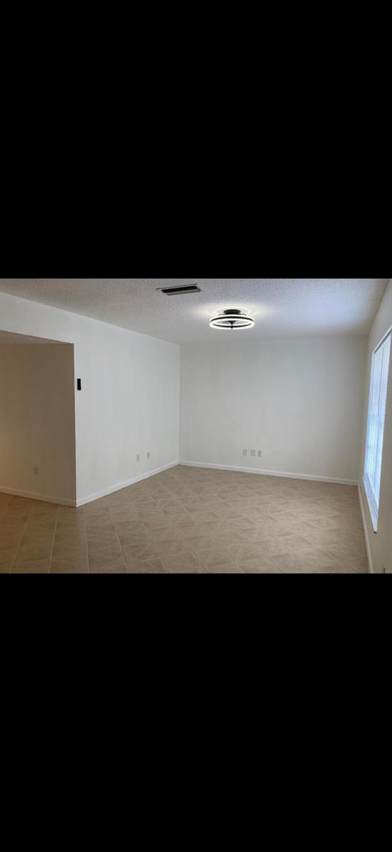 An empty room with white walls, tile flooring, and a modern circular ceiling light fixture — 1243 Kinglet Terrace, Wellington FL 33414, WELLINGTON, FL