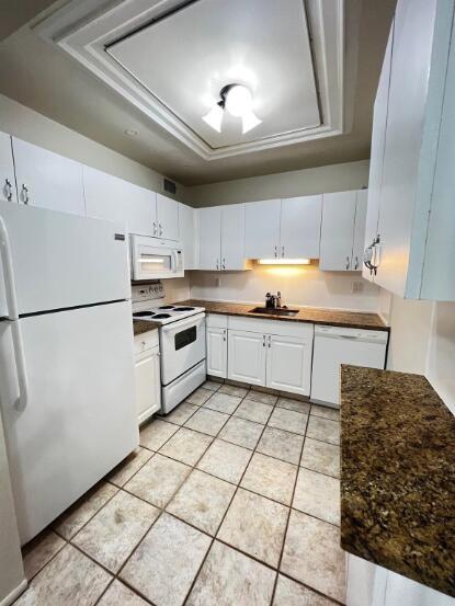 A kitchen with white cabinets, white appliances, dark granite countertops, and light-colored tile flooring — 6289 Lear Drive # 302, Atlantis FL 33462, ATLANTIS, FL