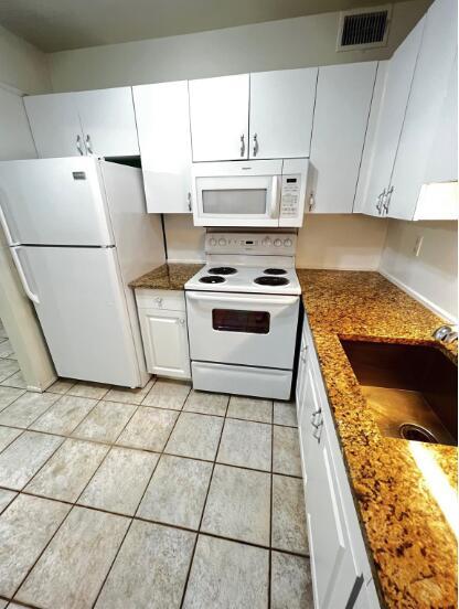 A kitchen features white cabinets, granite countertops, a white refrigerator, and a white electric stove — 6289 Lear Drive # 302, Atlantis FL 33462, ATLANTIS, FL