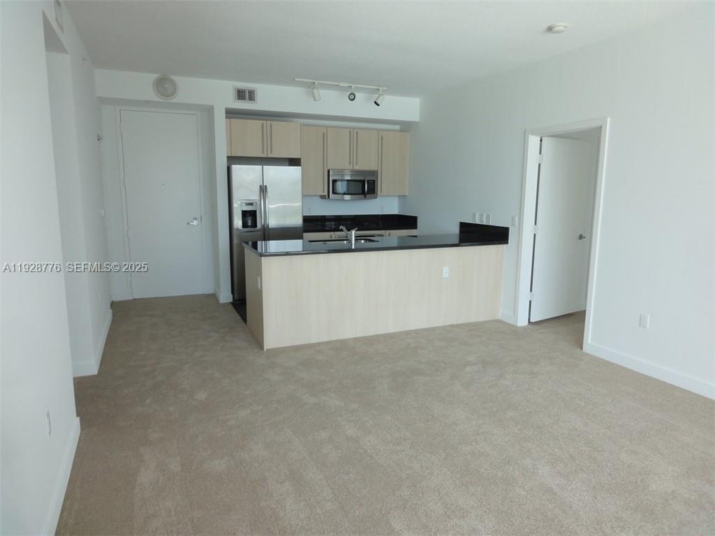 A kitchen with light wood cabinets and black countertops overlooks a carpeted living area — 79 SW 12th St # 1203S, Miami FL 33130, MIAMI, FL